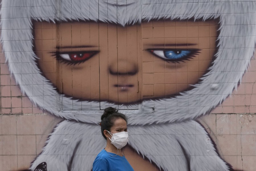 A person walks past a large mural of a face painted on a wall.
