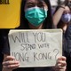 A woman wearing a face mask holds a placard reading, "Will you stand with Hong Kong?"