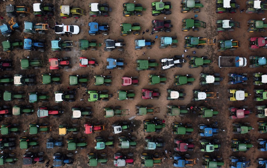 An aerial view of dozens of tractors parked end to end, filling a space during a protest.