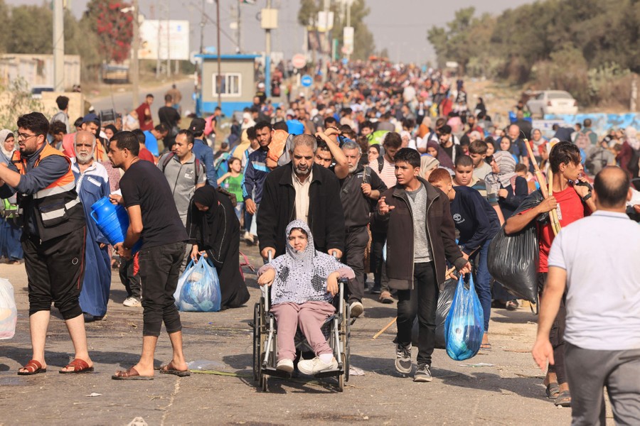 Large crowds of people flee holding plastic bags filled with their belongings.