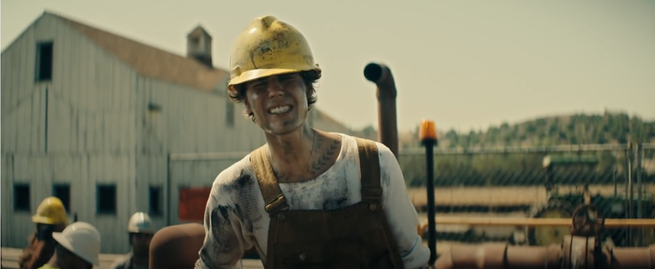 Justin Bieber, covered in mud, wears a yellow hard hat and Dickie's overalls and grimaces toward the viewer.