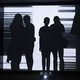 Four silhouettes in front of a projected black and white line pattern