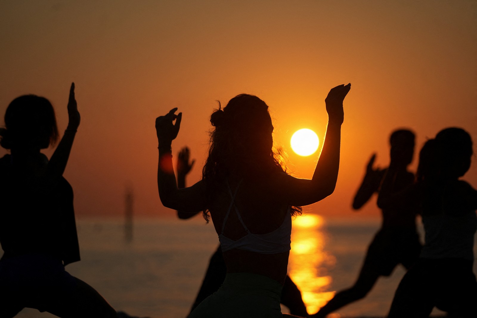 A group of people practice yoga during sunrise at the beach.