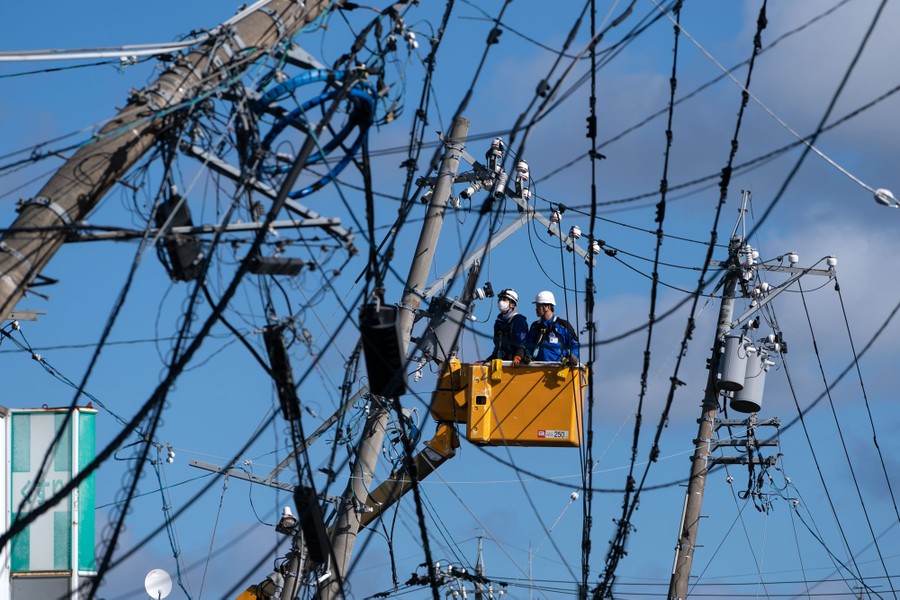 Two utility workers in a lift work on a tangle of electric power lines.