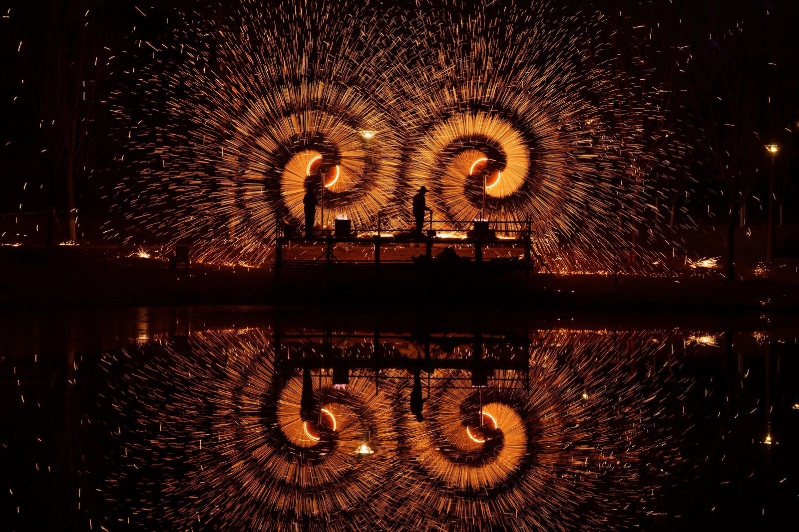 People on a stage send bits of molten iron flying from spinning mechanisms, making bright spiral shapes in the air.
