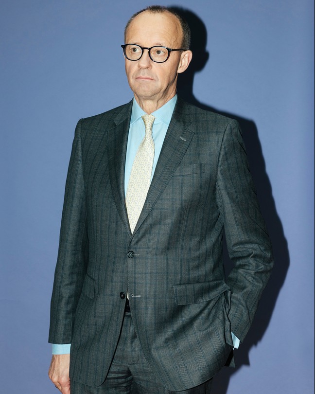 An unsmiling, vertical photo of Merz in a gray suit.