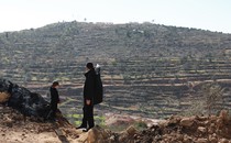A man stands on a hillside with a young boy, pointing into the distance
