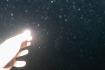 a brightly lit hand reaching out to the dark sky, the lens smudged with rain drops