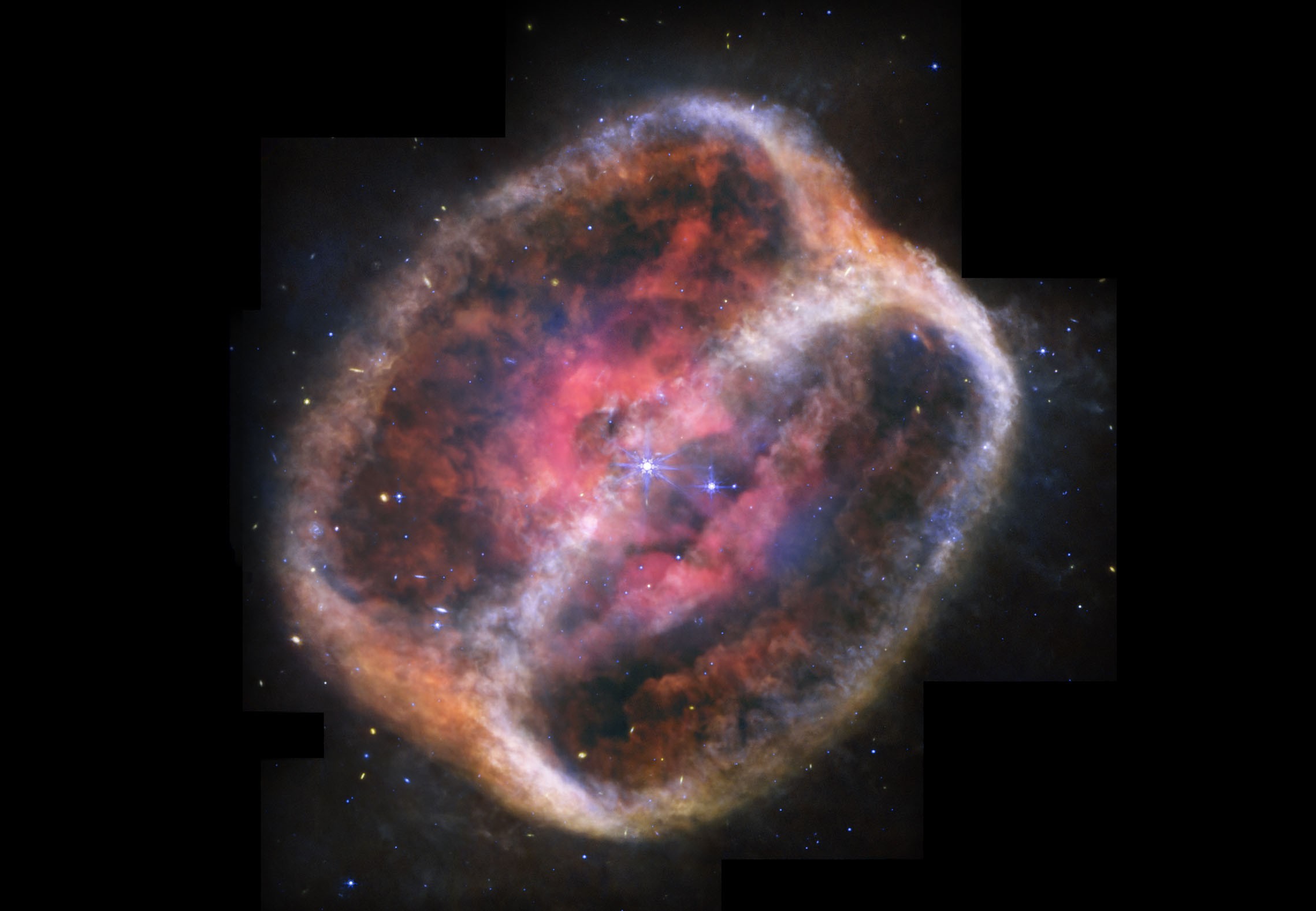 A giant shell of gas and dust surrounds a distant star. The shell is rounded and resembles red bell pepper that's been sliced in half.