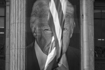 A banner with President Trump's image on it, hanging between building columns with an American flag flying between his eyes.