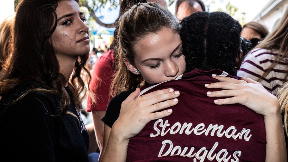 Young people hug. One is wearing a jacket that says "Stoneman Douglas" on the back.