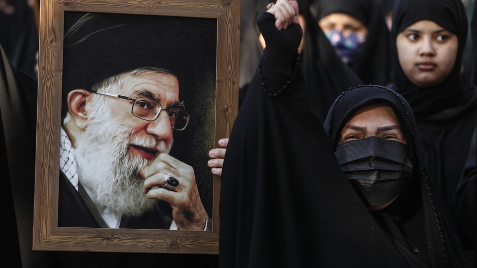 Women in chadors surround a large framed photograph of Ayatollah Ali Khamenei