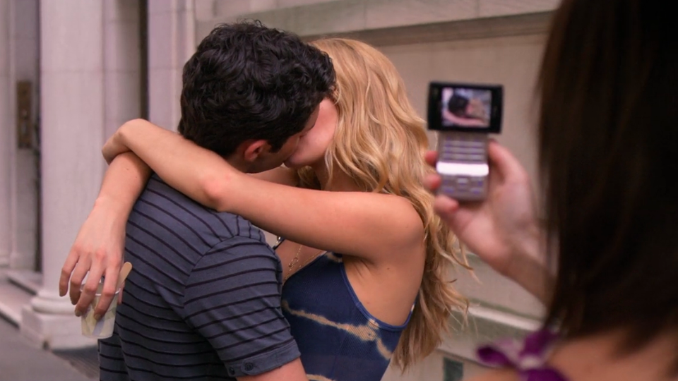 A person uses a cellphone to take a picture of a couple kissing.