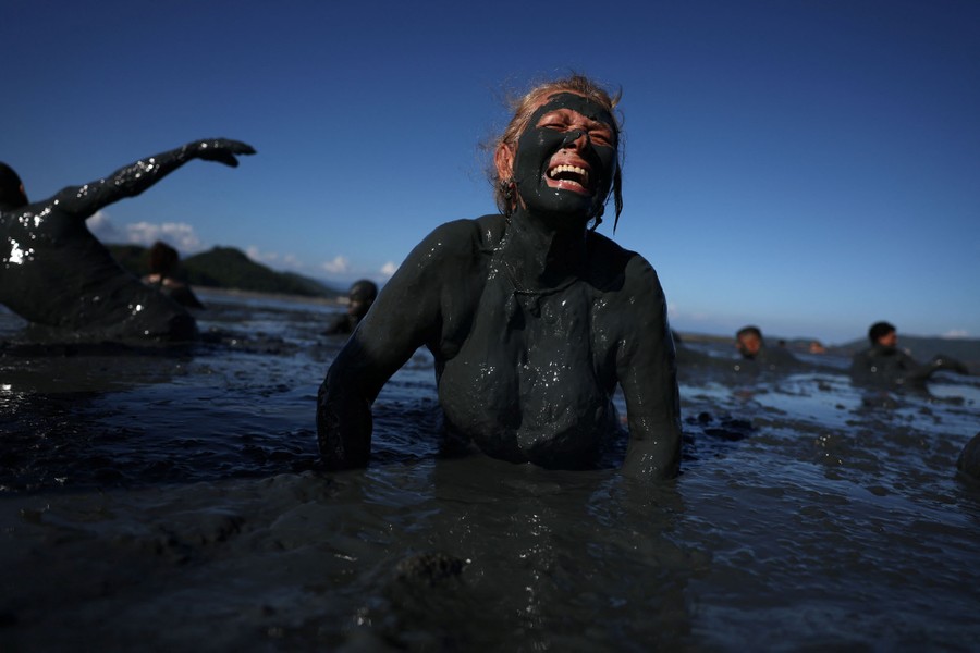 A woman, covered in dark mud, smiles while getting up from a mud patch.