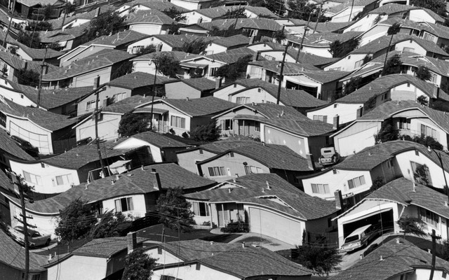 A warped black and white photograph of rows of houses in a neighborhood