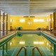 A blue swimming pool in a yellow tiled room with brown tiled columns