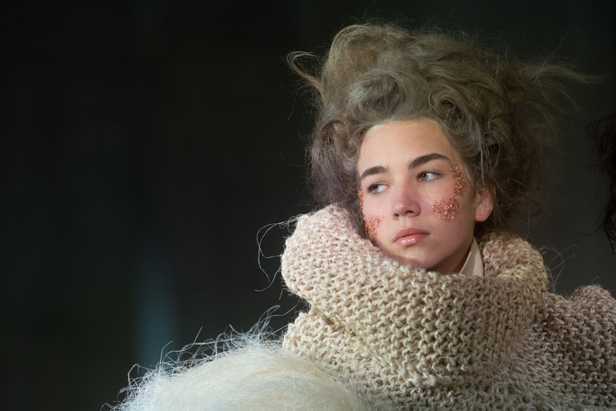 A model poses, wearing a large knit garment.