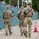 A color photograph of uniformed National Guard troops carrying guns while walking down a sidewalk in Washington, D.C.