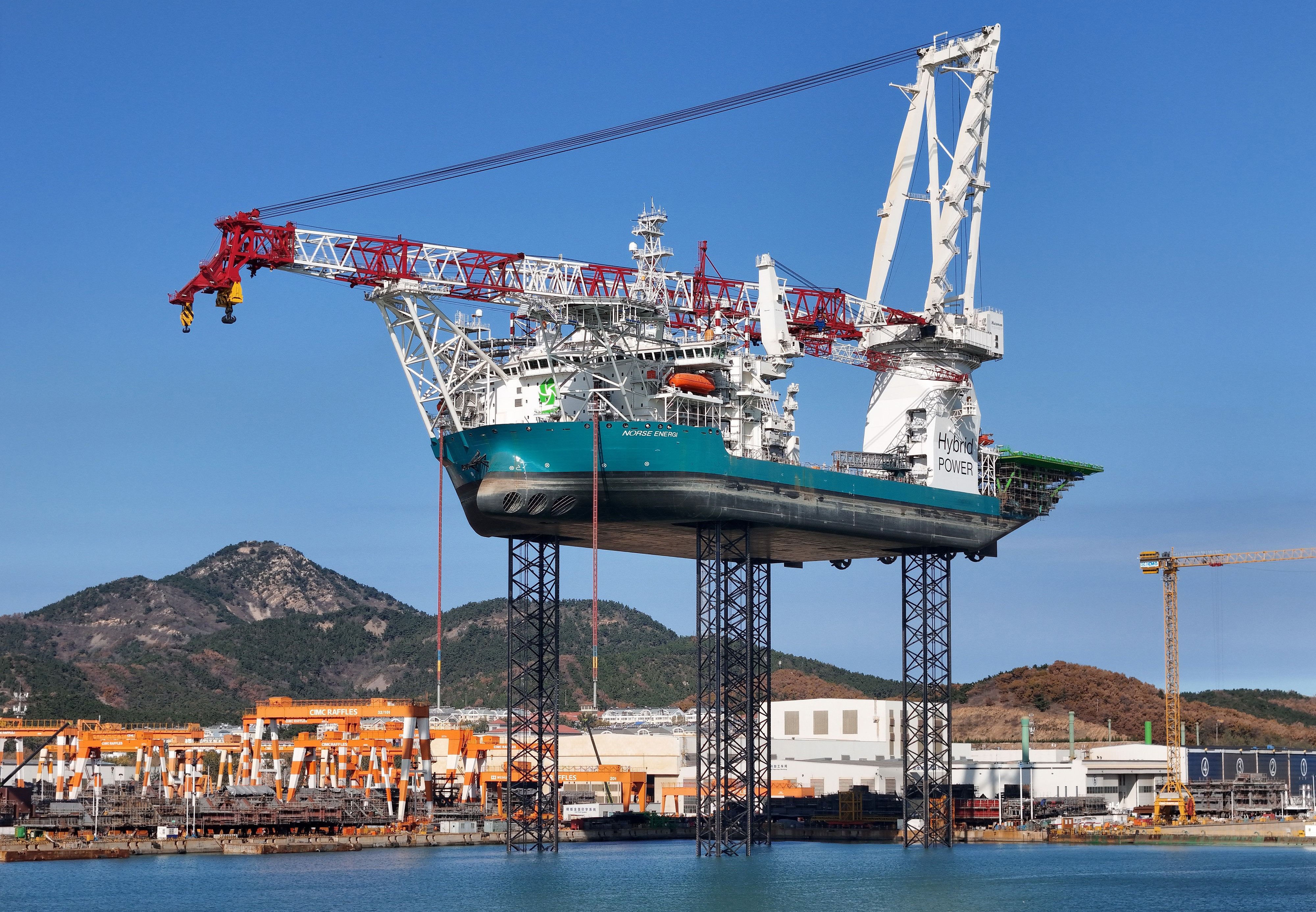 A large ship equipped with a tall crane, alongside a harbor, lifted high in the air on four tall jacks.