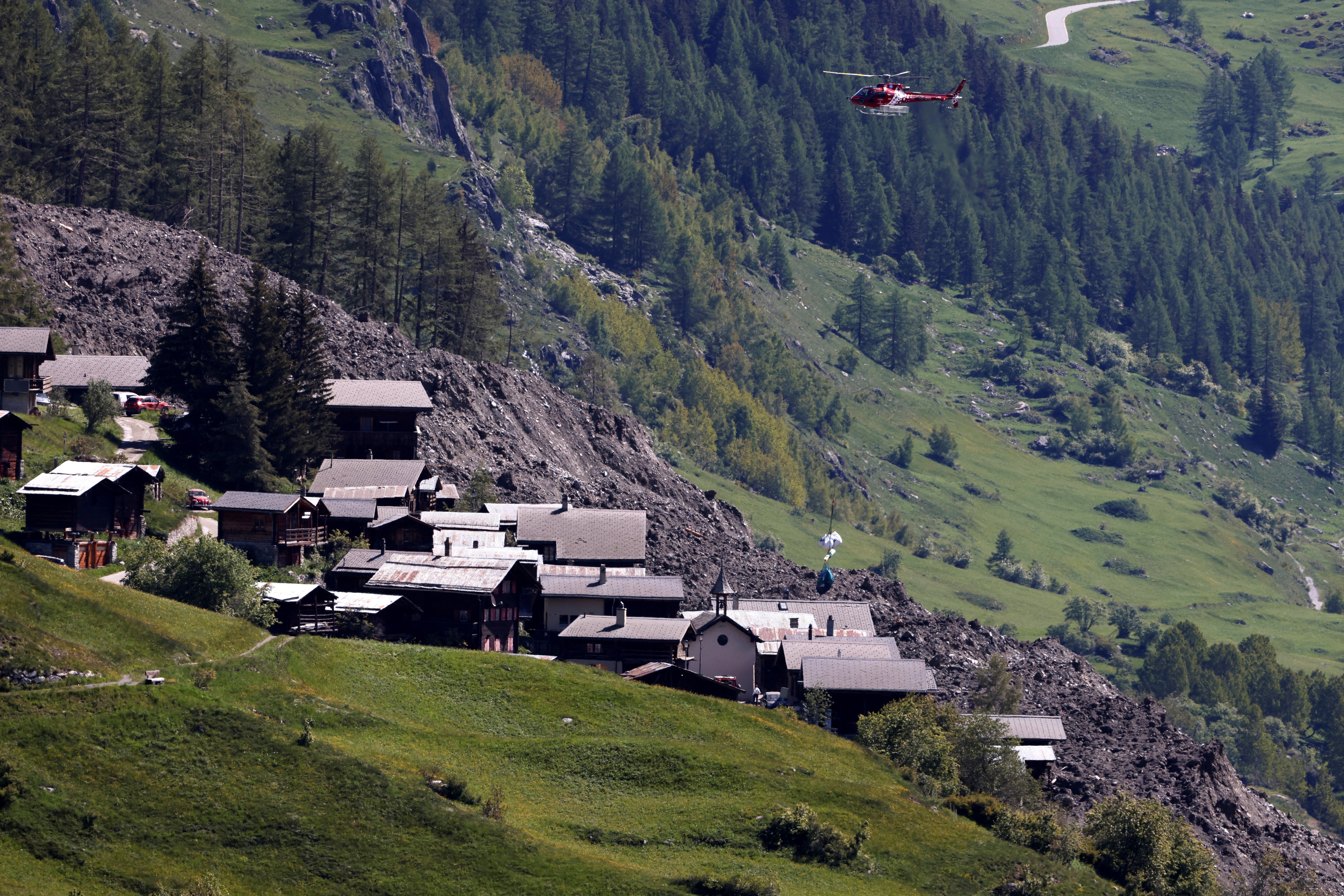 A helicopter lowers equipment to a village near a landslide.