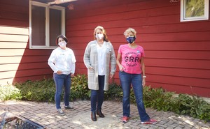 GRR's leader, Susan Polakoff Shaw, stands with two other women wearing jeans outside a red wood-paneled house.