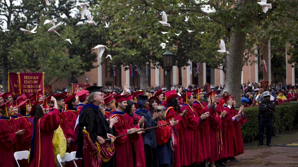 Doves fly over the heads of graduates dressed in deep red caps and gowns.