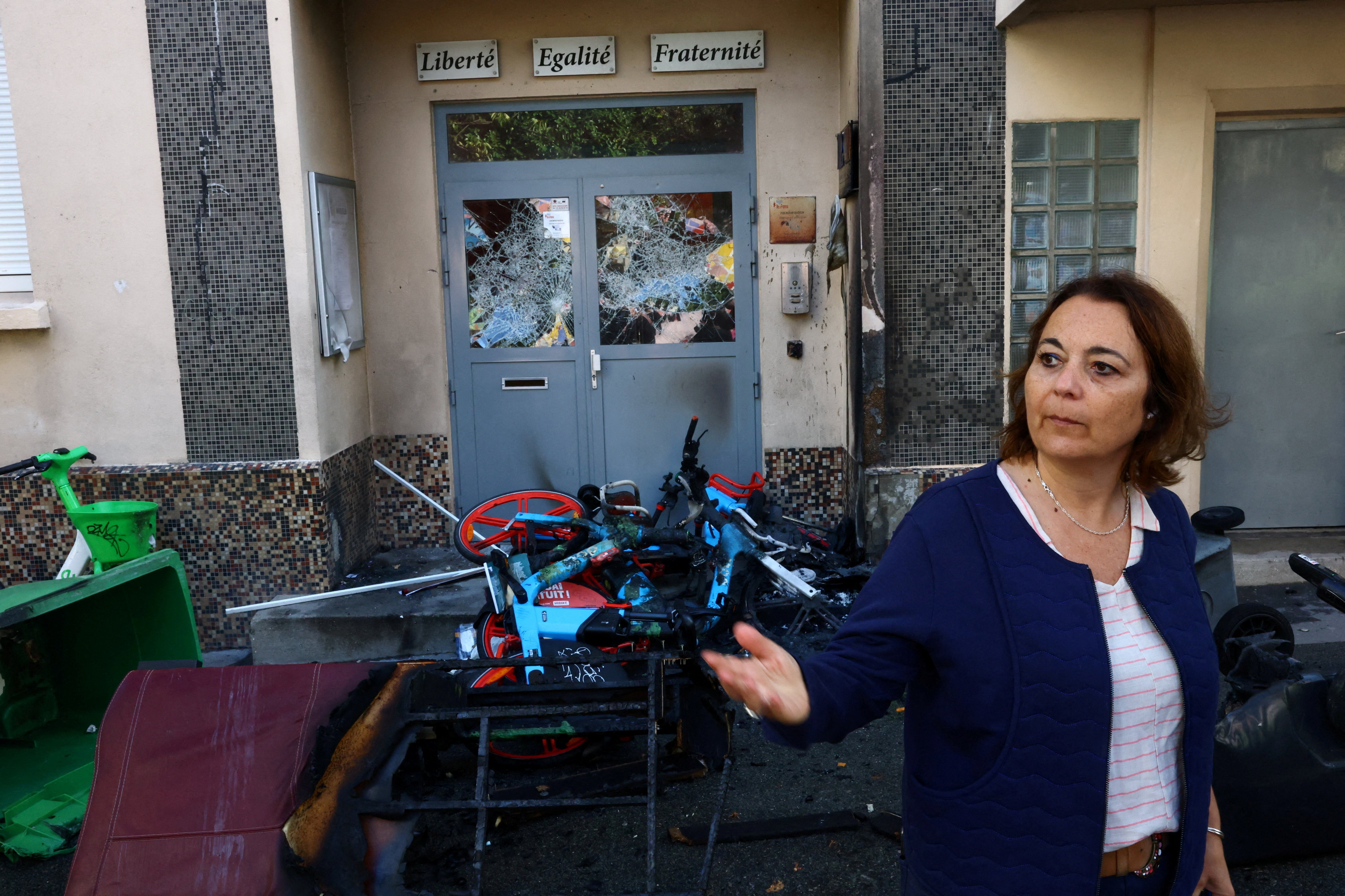 A high-school principal stands outside a school building beside damaged doors and debris, after a protest.