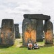 A photo of two protesters sitting in front of Stonehenge, which has orange spray paint on it