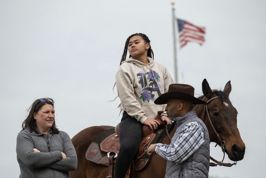 Two people stand beside a rider atop a horse.