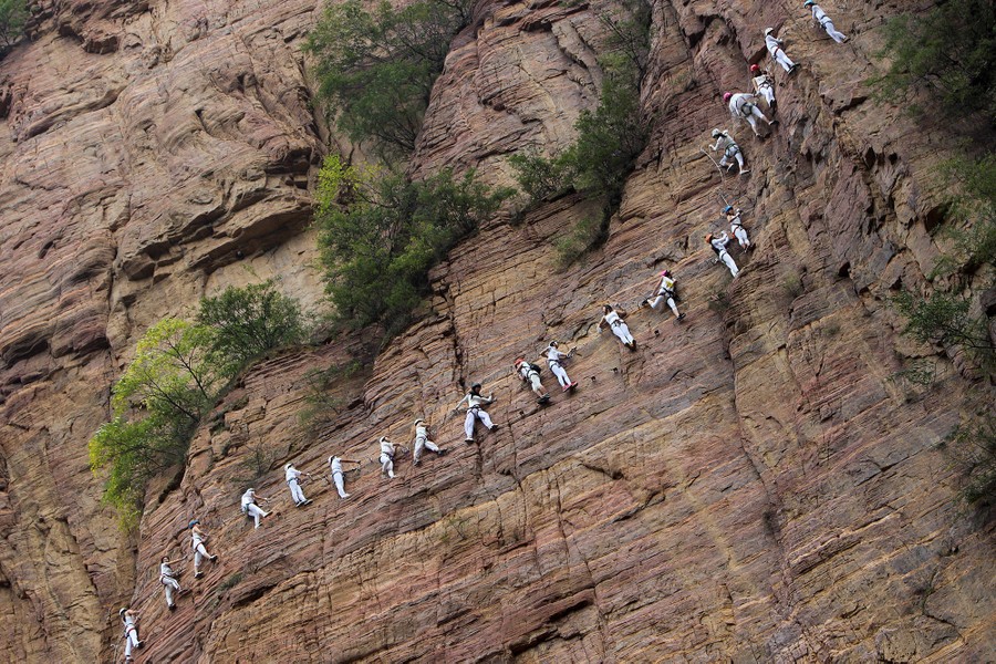 People move up a rope running along a rock face in the Qingyao mountains ou...