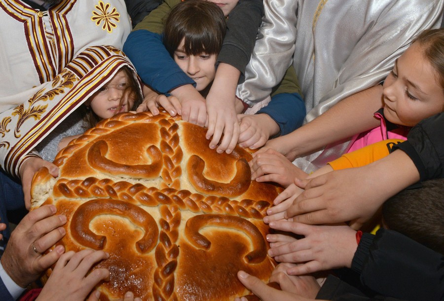 Children crowd around a large decorative loaf of bread, grabbing at its edges.