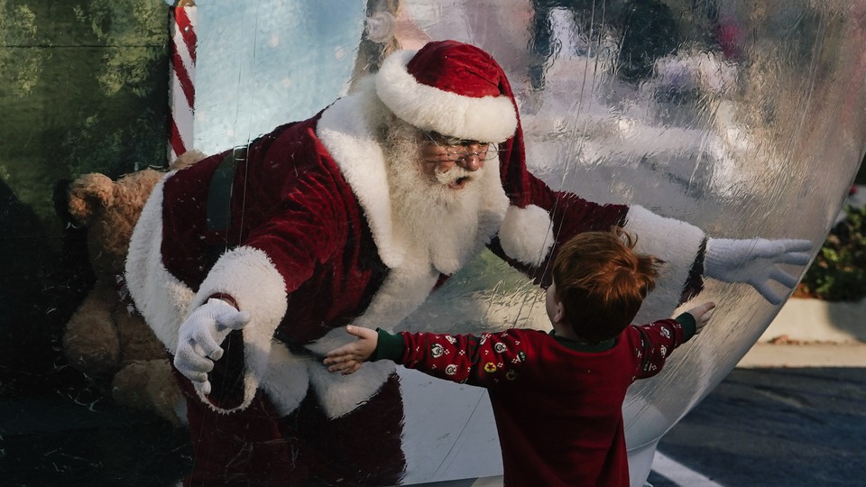 Santa Claus, entrapped in a giant snow globe, reaches out his hands towards a little boy, who also has his arms outstretched.