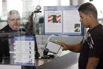 A traveler scans his fingerprints at the Houston airport as a customs officer monitors his computer.