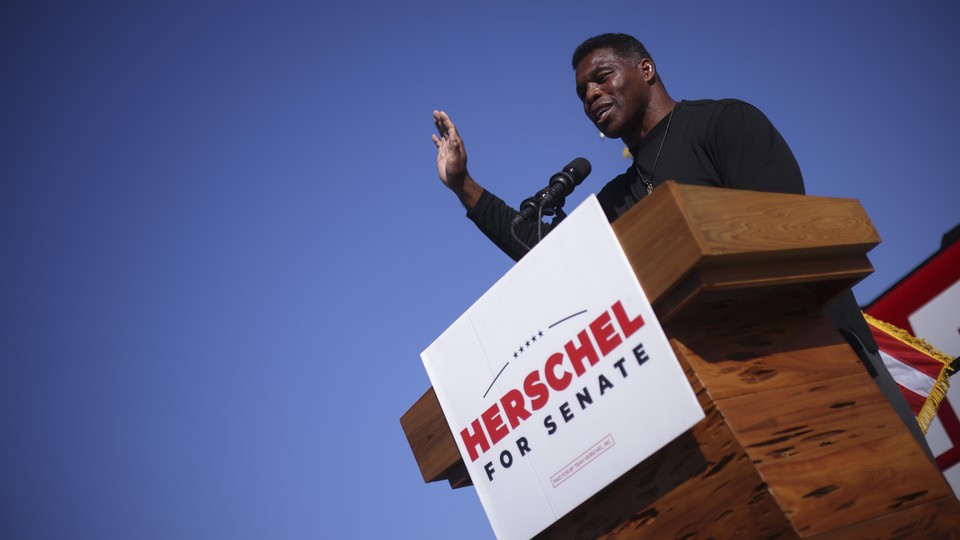 Herschel Walker stands at a lectern with his right hand in the air.
