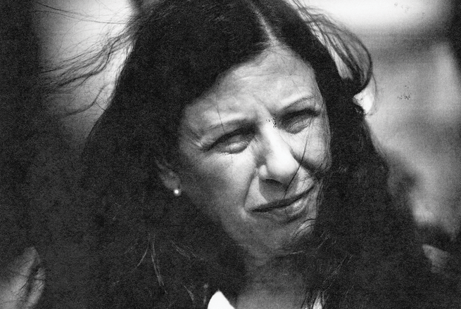 black and white photo of woman with dark windswept hair squinting in sunlight