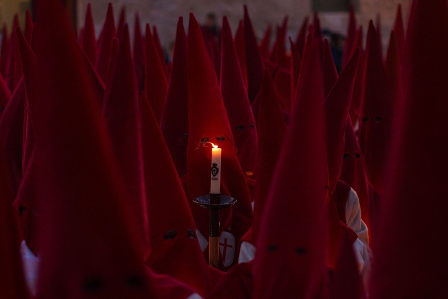 Dozens of Christians wearing tall red hoods gather together.