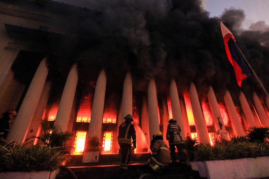 Firefighters douse a fire at a large multi-columned building.
