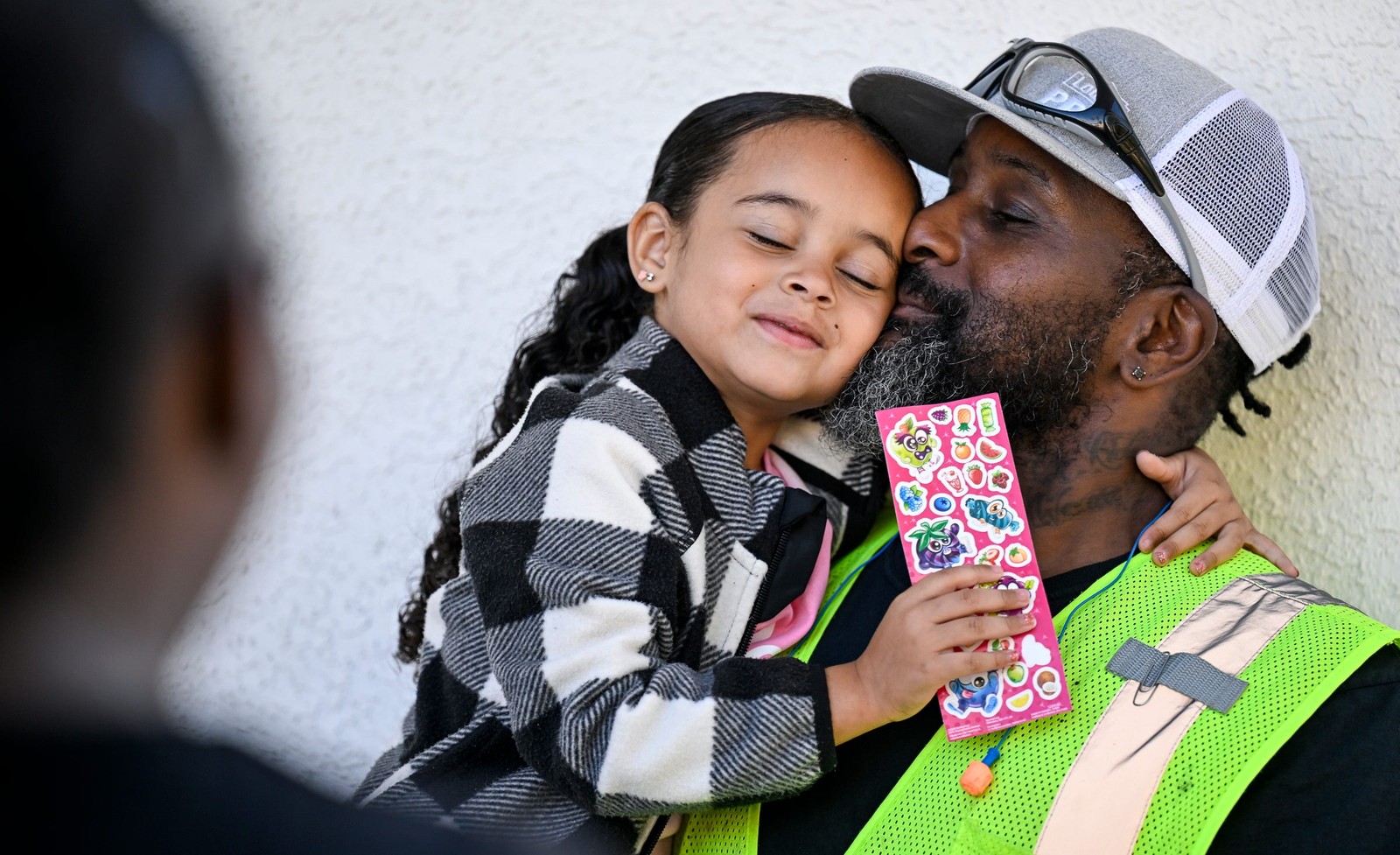 A father holds and kisses his young daughter on the first day of school.
