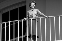 Nancy Reagan stands on a balcony, watching an unseen President Ronald Reagan depart the White House.