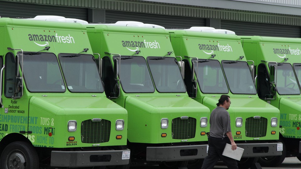Amazon Fresh delivery vans are lined up outside an Amazon warehouse