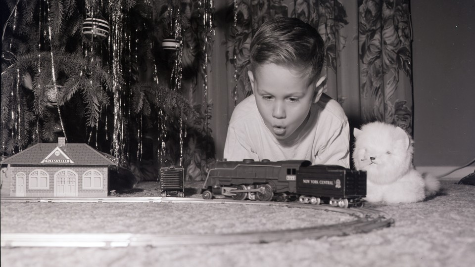 A boy looking at a toy railroad set by a Christmas tree