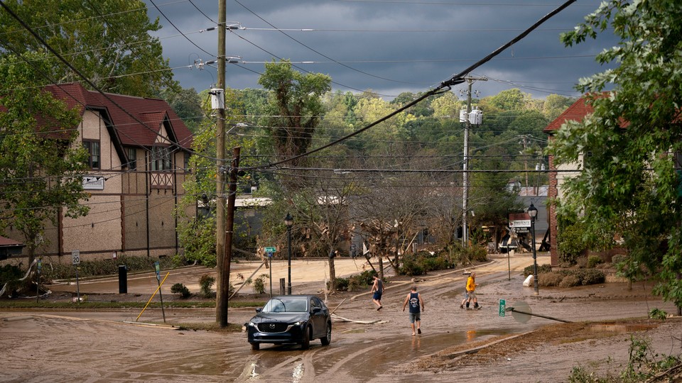 Four people walk across a muddy suburban street intersection and inspect flood damage in Asheville, North Carolina, after Hurricane Helene