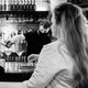 Two women sitting at a bar while a bartender pours a drink