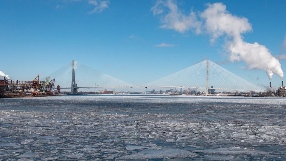 A huge bridge across an icy river, with smokestacks on both sides