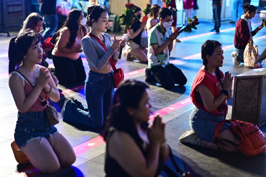 About ten people kneel and pray before a shrine.