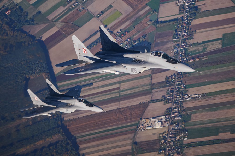 An aerial shot of two fighter jets flying above farm fields