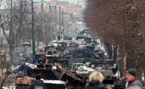 Several destroyed military vehicles sit in the middle of a road in a town.