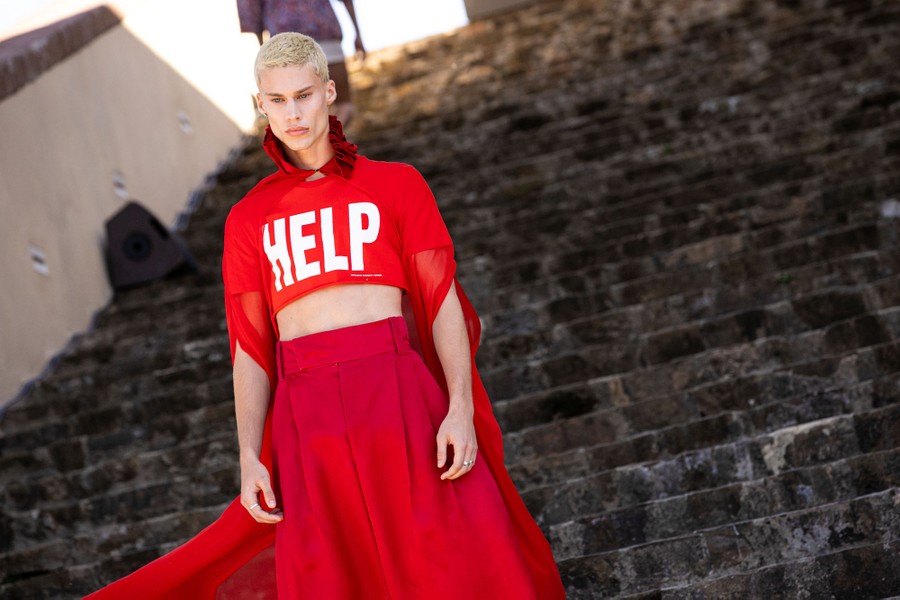 A model walks on a staircase wearing a red garment that has the word 'help' printed across the chest.