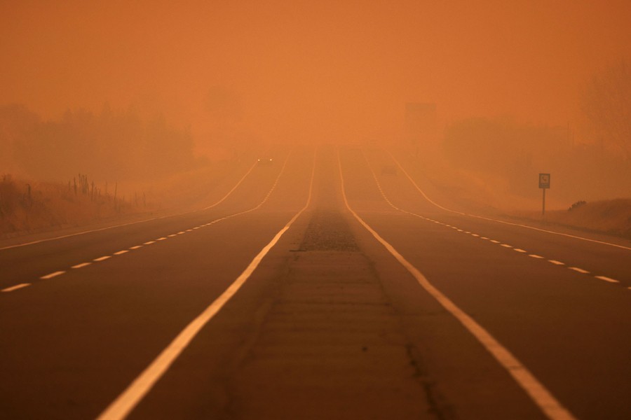 Smoke covers a road, coloring the sky orange.