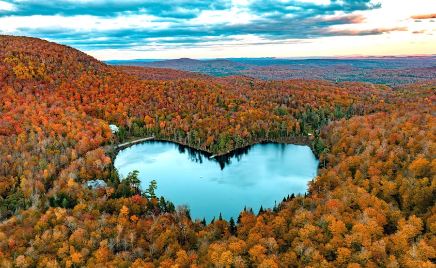 An aerial view of forested hills showing autumn colors, with a heart-shaped lake in the center.